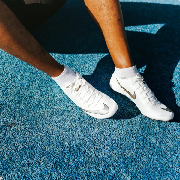 Close-up of an athlete's legs wearing Nike soccer cleats on a vibrant blue surface.